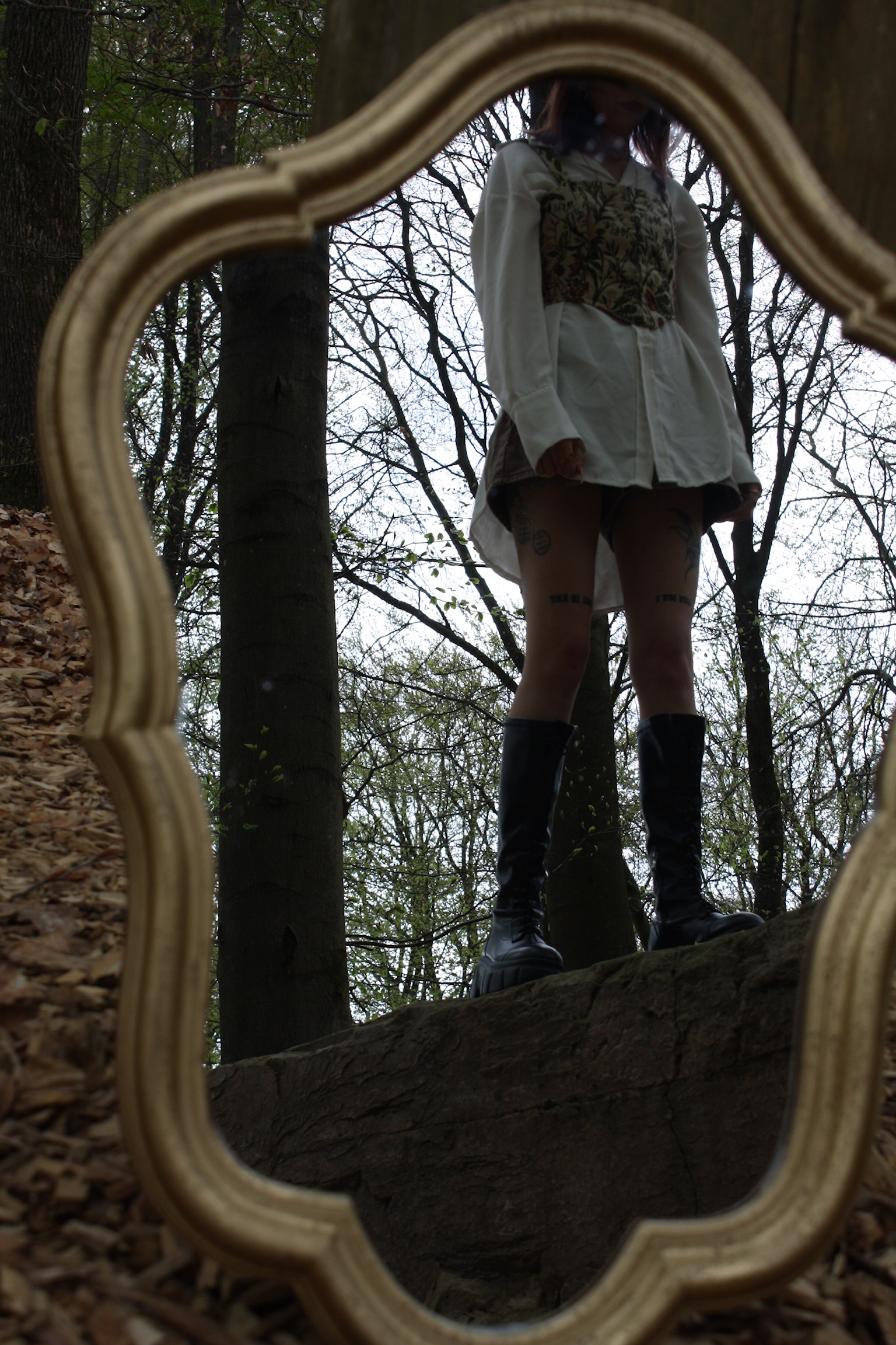 Jess reflected in a mirror in the forest, seen from below.